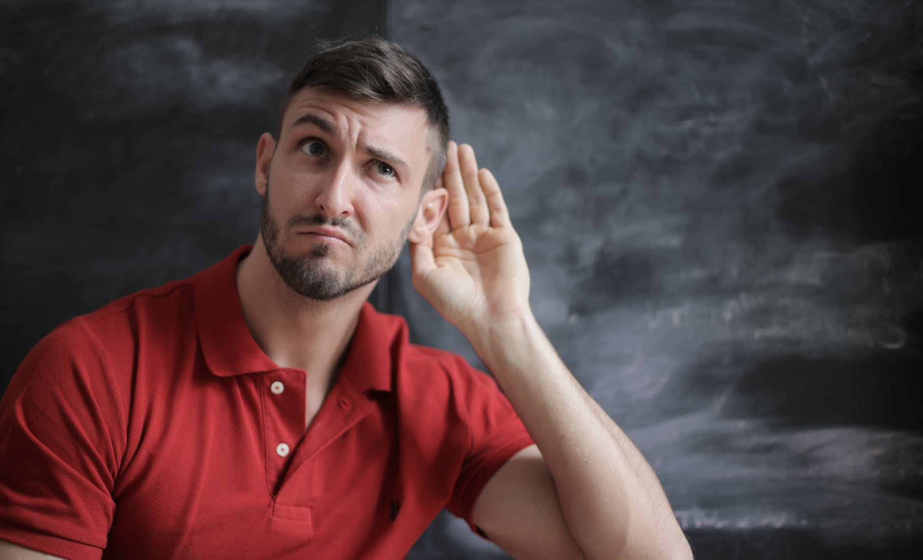 Listen man in red polo shirt sitting near chalkboard