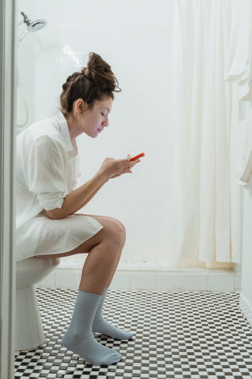 woman sitting on a toilet and using phone