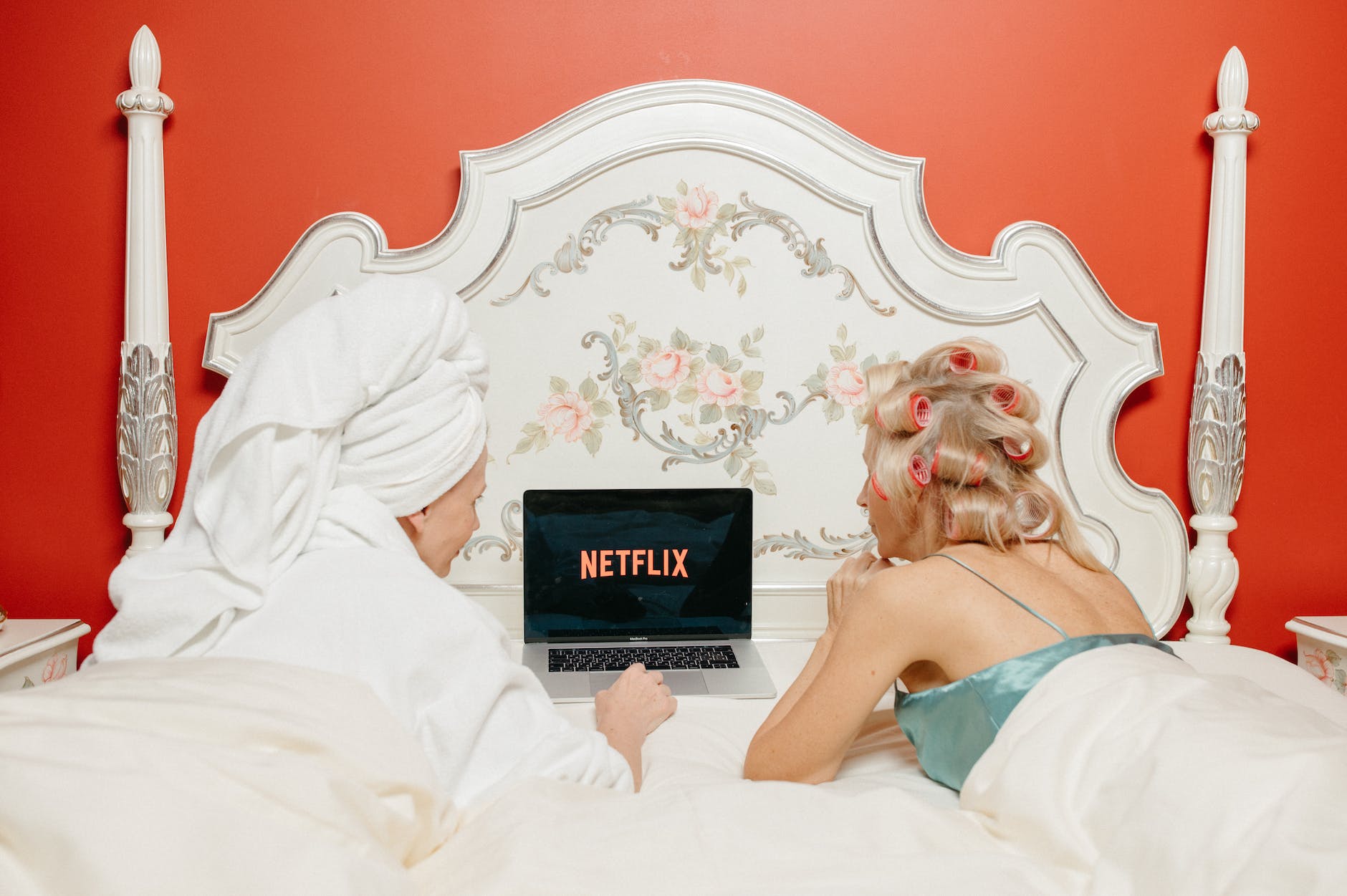 women lying on bed while looking Netflix at the screen of a laptop
