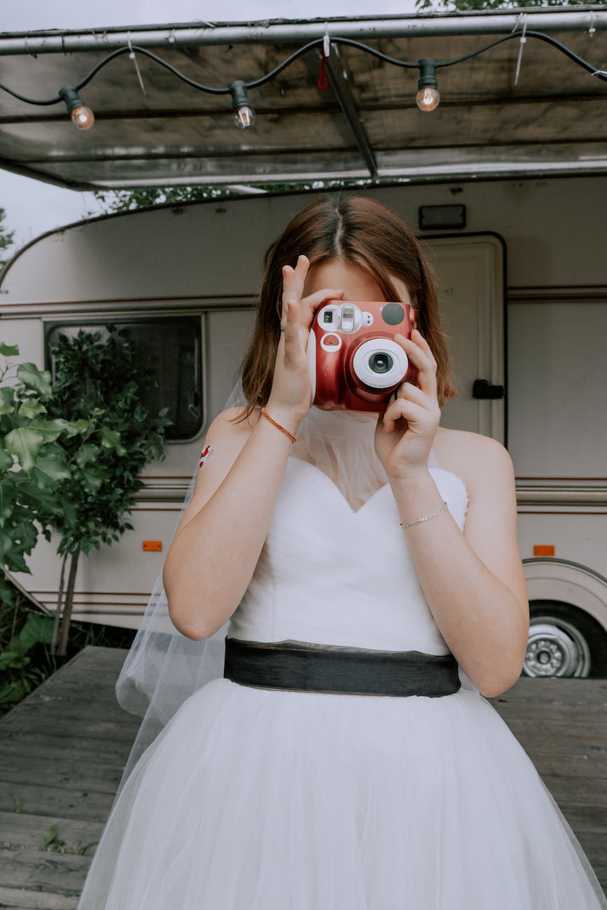 woman in white wedding dress holding red instant photo camera
